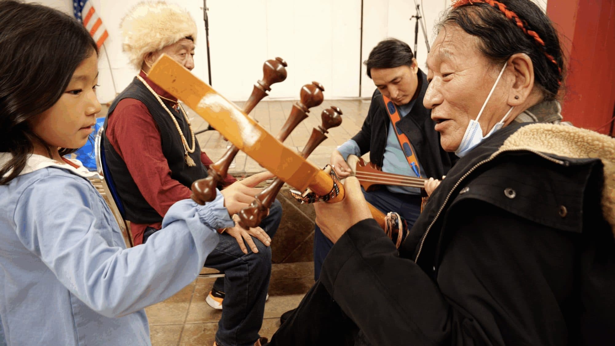 An elder musician places a dranyen in a young girl's hands